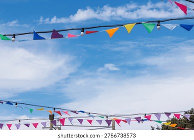 Rows of colorful triangular bunting flags hanging outdoors against a bright blue sky with soft clouds. Background with copy space