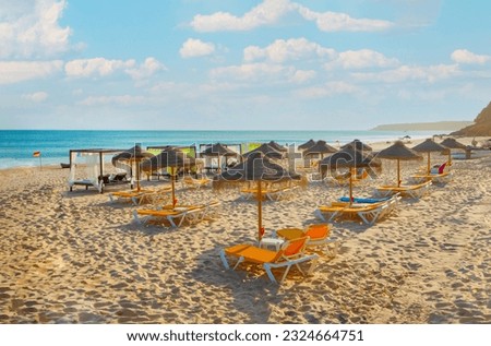 rows of deck chairs and umbrellas on sandy beach along Algarve in Portugal. Sommer travel concept and beach background