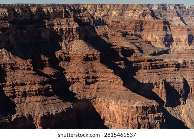 Rows of deep red and rust-colored cliffs recede toward the horizon at the Grand Canyon's South Rim, Arizona, USA, beneath a pale blue sky on a clear autumn afternoon.