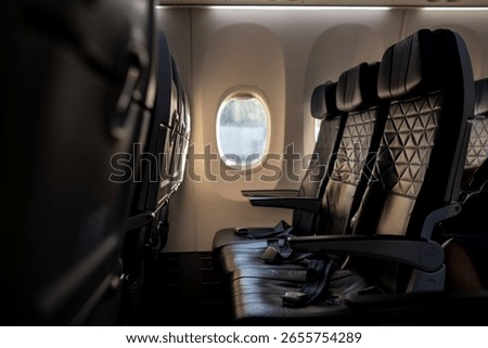 Rows of empty airplane seats offer a view of fluffy clouds through the window, showcasing the tranquility of flight at sunset.