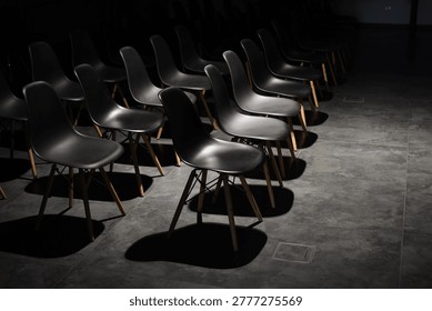 Rows of empty black chairs in dimly lit conference hall. Selective focus