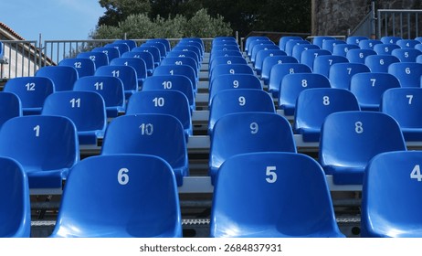 Rows of empty blue stadium seats numbered from one to twelve, arranged in a neat pattern under a clear blue sky, creating a sense of anticipation for an upcoming event