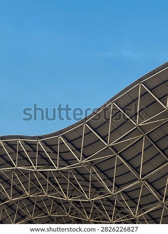 Rows of empty blue, white, and plastic seats in an outdoor sports stadium stand under a roof structure.