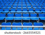 Rows of empty bright blue plastic seats in the grandstand of an outdoor stadium create a repeating graphic pattern.