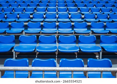 Rows of empty bright blue plastic seats in the grandstand of an outdoor stadium create a repeating graphic pattern.