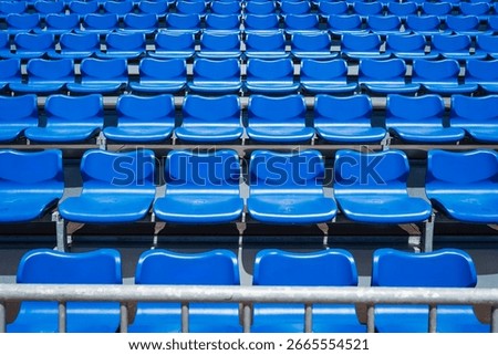 Rows of empty bright blue plastic seats in the grandstand of an outdoor stadium create a repeating graphic pattern.