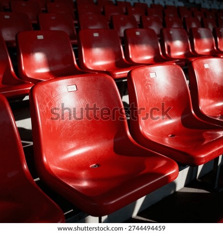 Rows of empty, bright red stadium seats arranged in a tiered formation, showing texture and signs of wear in the sunlight