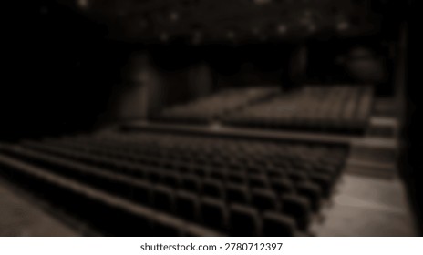 Rows of empty dark seats fill a theater auditorium with overhead stage lighting visible in the dimly lit interior.