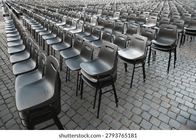 Rows of empty gray plastic chairs arranged outdoors on cobblestone pavement, ideal for event seating, ceremony setup, or conference preparation