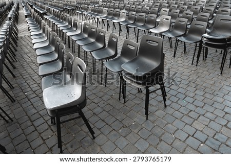 Rows of empty gray plastic chairs arranged outdoors on cobblestone pavement, ideal for event seating, ceremony setup, or conference preparation