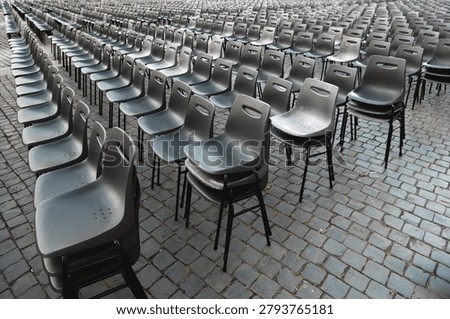 Rows of empty gray plastic chairs arranged outdoors on cobblestone pavement, ideal for event seating, ceremony setup, or conference preparation