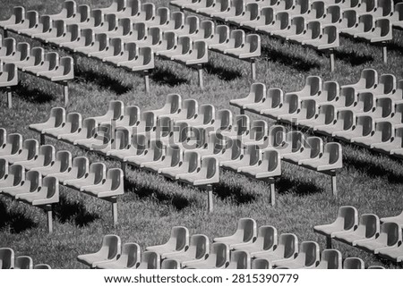 Rows of empty outdoor stadium seats on grass, creating a repeating pattern and geometric texture in black and white.