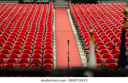 Rows of empty red chairs prepared for a large event, ceremony, graduation, inside an arena. Wide view