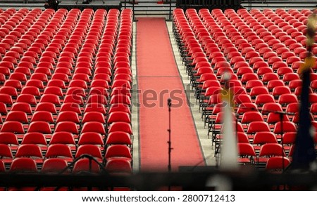 Rows of empty red chairs prepared for a large event, ceremony, graduation, inside an arena. Wide view