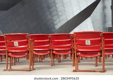 Rows of empty red seats await spectators against the striking, abstract backdrop of a contemporary building exterior