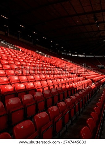 Rows of empty red seats in a massive sports stadium stand in dramatic lighting under a dark roof before a major game event.