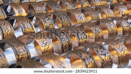Rows of engraved copper cuff bracelets with ornate motifs displayed at an artisan market, showcasing handmade metalwork and traditional jewelry.