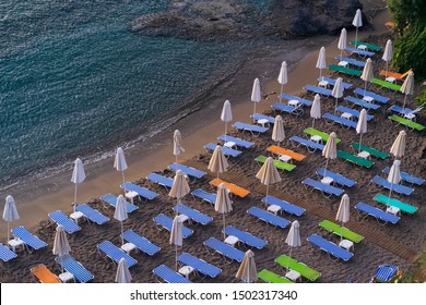 Rows of folded  beach umbrellas  and  empty sunbeds on the beach, early morning. Crete, Greece. Top view. Travel and leisure concepts.