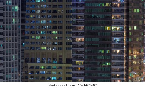 Rows of glowing windows with people in the interior of apartment buildings at night. Modern skyscrapers with glass surface. Concept for business and modern life. Tilt up