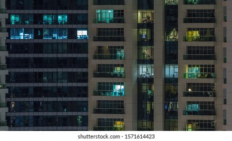 Rows of glowing windows with people in the interior of apartment building at night. Modern skyscraper with glass surface. Concept for business and modern life. Pan left