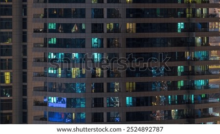 Rows of glowing windows with people in the interior of apartment building at night. Modern skyscraper with glass surface. Concept for business and modern life