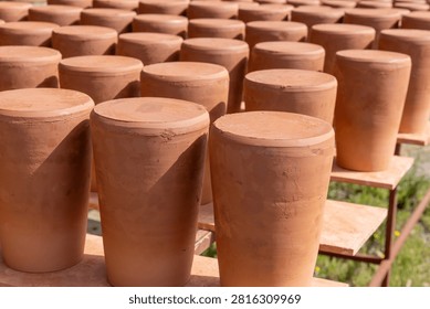 Rows of hand-formed clay pots are drying naturally on wooden shelves under sunlight