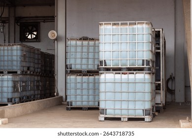 Rows of intermediate bulk containers (IBCs) filled with a light blue liquid, likely water or industrial fluid, stacked on pallets in a warehouse or factory setting.