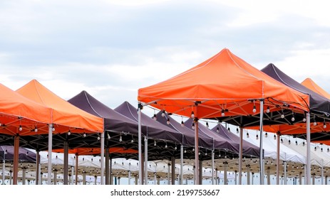 Rows of many foldable canopy Tents with hanging LED light bulbs decoration for outdoors Event against cloudy sky background