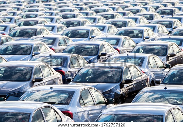 Rows of a new cars\
parked in a distribution center on a car factory on a sunny day.\
Parking in the open air.