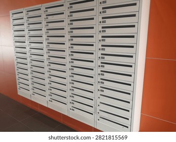 Rows of Numbered Mailboxes in Apartment Lobby Large wall-mounted array of secure metal mailboxes in a modern apartment building lobby with orange tiled walls.