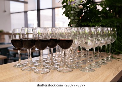 Rows of red wine filled and empty glasses organized on a wooden table ready for party or event serving.