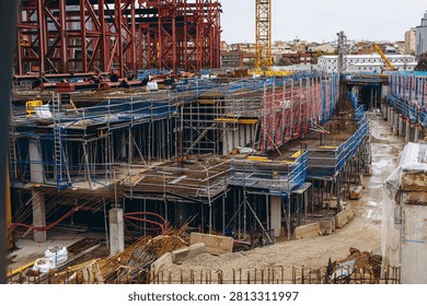 Rows of scaffolding and blue formwork line a deep excavation at an urban building site. Foundation work and site safety supporting civil engineering and construction equipment markets.
