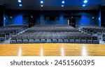 Rows of seats, grey chairs in empty auditorium. School and University convention hall with lights on, reflection on the laminate stage. A venue for concerts, conferences, performances, plays, seminars