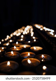 Rows of small candle lights, lighting in the dark background of religion church, make merit, pray, respect, peaceful and religion concept