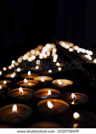 Rows of small candle lights, lighting in the dark background of religion church, make merit, pray, respect, peaceful and religion concept