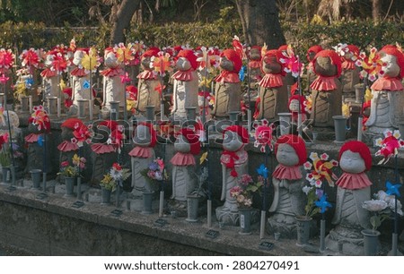 Rows of small stone Jizo statues wearing red knitted caps and bibs decorated with colorful pinwheels at a Japanese cemetery
