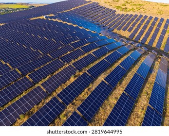 Rows of solar panels are installed in a large area. The sun shines on the panels, generating electricity. The scene shows a green landscape in the background.