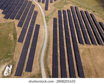 Rows of solar panels stretch across a field with a road running through. The bright sun shines down on the panels as they capture energy.