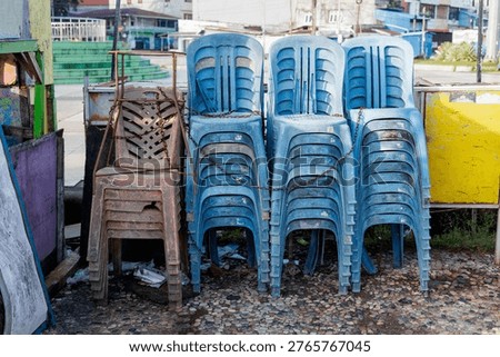 Rows of stacked blue and brown plastic chairs secured with a rusty metal chain at a street stall