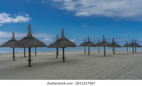 Rows of straw umbrellas on a sandy beach without people. White sand, turquoise ocean, blue sky, clouds. Mauritius. Hotel. Resort.