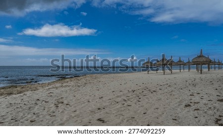 Rows of straw umbrellas on a sandy beach without people. Calm turquoise ocean, white sand, blue sky, clouds. Mauritius. Hotel. Resort. Low season.