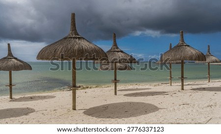 Rows of straw umbrellas on a sandy beach without people. Round shadows on white sand. A calm turquoise ocean. Blue sky, clouds. Mauritius. Resort. Hotel.