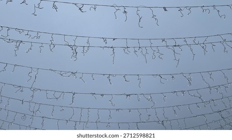 Rows of stretched light cables and disconnected garland against a clear blue sky outdoor urban holiday decoration