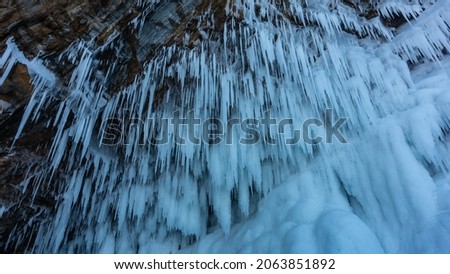Rows of thin long stalactite icicles hang from the ceiling of the cave. Close-up. Full screen. Baikal