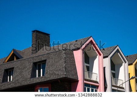 Rows of triangular elements of roofline covered with shingle, with chimney against blue sky