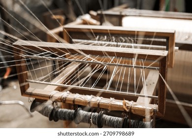 Rows of warp threads stretched across a wooden frame as part of the weaving setup. The scene shows careful preparation in textile production.