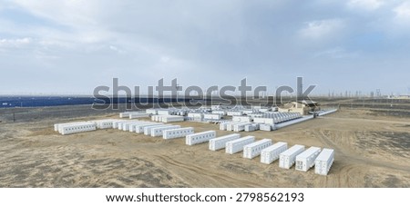 Rows of white containerized battery units deployed across arid Gobi terrain, adjacent to solar farms and transmission infrastructure under overcast sky, Gansu province, China.