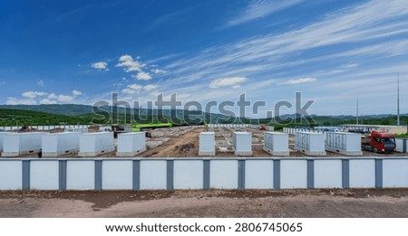 Rows of white containerized battery units installed on concrete pads at an active construction site, with mountains and clear sky in background,  Ningxia, China