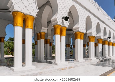 The rows of white pillars at the Sheikh Zayed Grand Mosque in Solo, adorned with gold ornaments and majestic arches, create a beautiful architectural corridor, reflected in the marble floor.