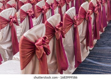 Rows of White Satin Slipcovered Chairs with Pink Ribbon Bows tied around them for a Wedding Ceremony